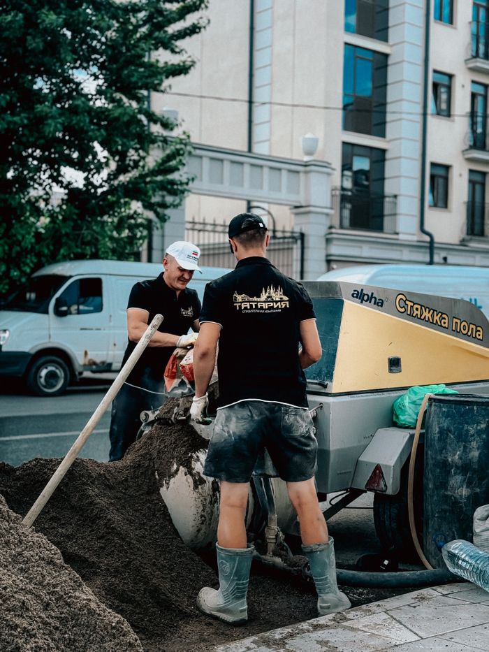 Two male construction workers operate a cement mixer on an urban street.